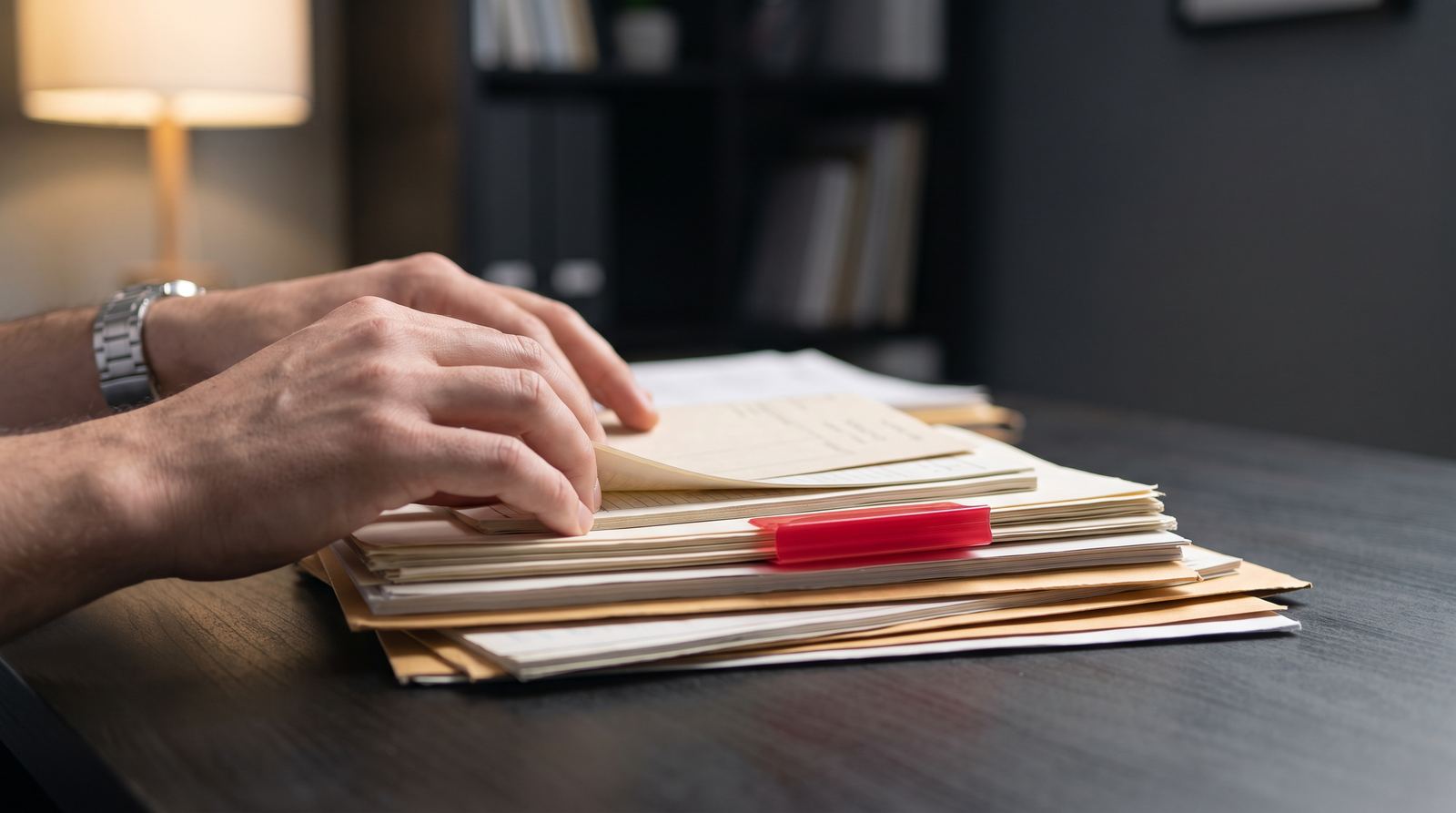 Manos organizando expedientes contables sobre un escritorio, con un separador rojo como único acento de color